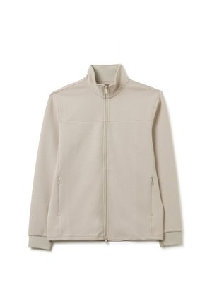 Lichtbeige zip-up jas van zacht materiaal. Voorzien van een hoge kraag, twee zijzakken en ribgebreide manchetten voor een nauwsluitende pasvorm. Glad textuur.