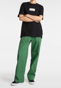 T-shirt noir à manches courtes avec un logo Vans ; associé à un pantalon large vert ; baskets classiques ; design simple, en coton.