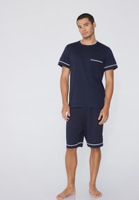 Ensemble de pyjama à manches courtes bleu marine fabriqué en tissu doux, avec un bord de poche blanc et un short assorti doté d'une taille élastique.