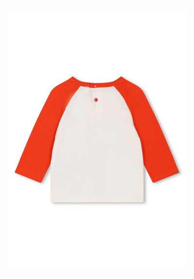 Chemise à manches longues avec un corps blanc et des manches raglan rouges vives, dotée d'une fermeture à bouton à l'arrière et d'une texture lisse et douce.