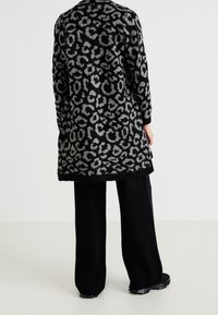 Cardigan largo con estampado de leopardo en negro y gris, de corte relajado, textura de punto y puños acanalados. Combinado con pantalones de pierna ancha en negro.