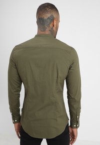 Olivenfarvet langærmet skjorte med en tætsiddende pasform, knapmanchetter og minimal dekoration; glat tekstur og lige kant bagpå.