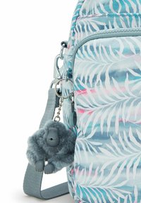 Rugzak met een lichtblauw tropisch bladerenpatroon, voorzien van een grijs fuzzy gorilla-sleutelhanger, zilveren hardware en een gestructureerde schouderriem.