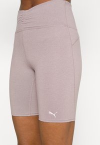 Světle mauve sportovní šortky s vysokým pasem, texturovanou tkaninou a nabíraným detailem na pase. Na stehně se nachází bílá značka.