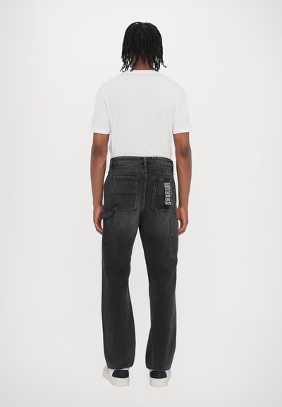 Pantalons cargo en denim noir avec une coupe décontractée, plusieurs poches et un détail logo subtil à l'arrière. Associés à un t-shirt blanc.