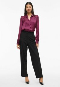 Blusa de satén en color ciruela con frente abotonado y mangas gather, combinada con pantalones de pierna ancha de talle alto en negro y tacones negros de punta.