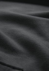 Detailní záběr tmavošedé látky ukazující měkkou texturu a jemný pletený vzor s jemnými záhyby a stíny.