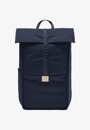 Mochila de tela azul marino con parte superior enrollable y cierre de hebilla, que presenta una forma rectangular, un bolsillo frontal y un pequeño parche de logo en color beige.
