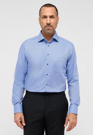 Hellblaues Button-Up-Hemd mit kleinem Karomuster, langen Ärmeln, einer einzigen Brusttasche und schwarzen Knöpfen. Getragen mit schwarzen Hosen.