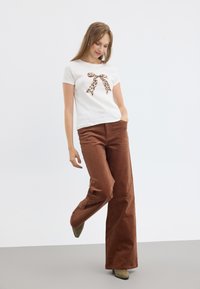 Bijela T-shirt s kratkim rukavima i detaljem mašne u leopard printu, uparen s smešnim širokim hlačama od kordura i maslinasto zelenim petama.