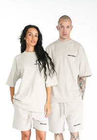 Béžové bavlněné oversized trička s krátkým rukávem a odpovídajícími šortkami, s předním logem "MULTIPLY" v černé barvě. Hladká textura, ležérní design.