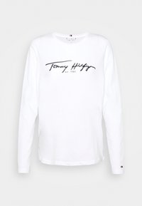 T-shirt bianco a maniche lunghe in cotone, con testo logo in corsivo nero e un piccolo accento colorato sulla manica.