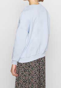 Felpa azzurra chiaro in misto cotone, con scollo rotondo, spalle ribassate e polsini a costine, abbinata a una gonna con motivo floreale.