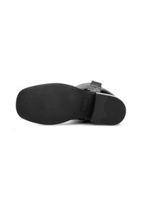 Suela de zapato de goma negra con un patrón texturizado, forma curvada y un recorte rectangular cerca del talón. Bordes suaves y sin signos visibles de desgaste.