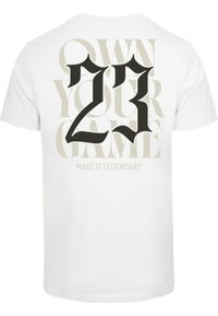 T-shirt en coton blanc avec un grand graphique noir "23" et le texte "OWN YOUR GAME" en beige tonal derrière, avec "MAKE IT LEGENDARY" en dessous.