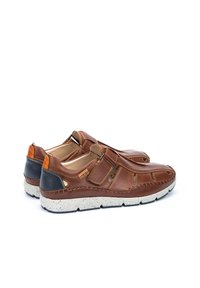 Zapatos marrones de cuero tipo slip-on con cortes, que presentan acentos en color camel y negro, una suela blanca moteada y detalles de costura en contraste.