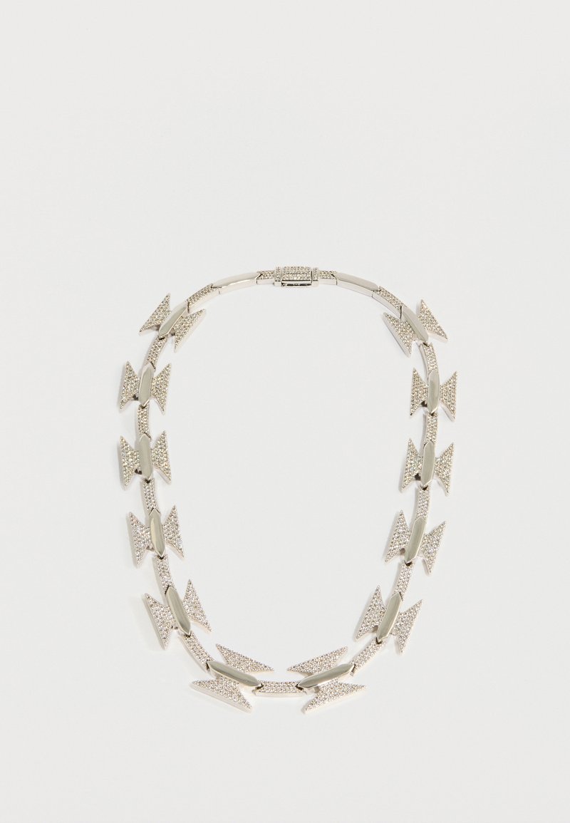 Srebrna ogrlica z izmeničnimi oblikami puščic in gladkimi členki, pri čemer so nekatere puščice okrašene z majhnimi prozornimi kristali za dodaten detajl.