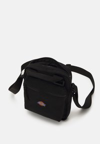 Geantă neagră tip crossbody din nailon, cu un compartiment principal cu fermoar, buzunar frontal și patch cu logo țesut. Include un breteau ajustabil.