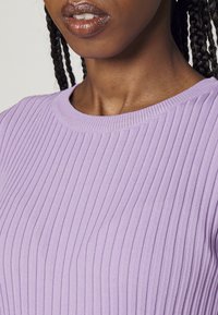 Haut en maille côtelée violet clair avec un col rond, présentant de fines rayures verticales et une texture douce. Vue en gros plan du col et des épaules.