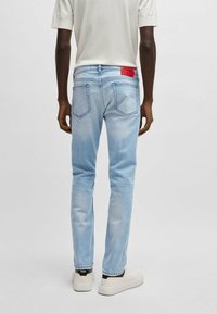 Blugi din denim bleu deschis cu o croială slim, având o etichetă roșie pe spate, cusături în contrast și minimalisme.