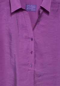 Camicia button-up viola con colletto, cinque bottoni frontali e una texture leggermente stropicciata. L'etichetta riporta "Creative Getaway."