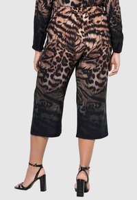 Kalhoty ve stylu culotte s leopardím potiskem v hnědé a černé barvě, vybavené elastickým pasem a lehkým, hladkým materiálem. V kombinaci s černými sandály na podpatku.