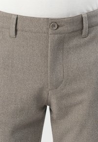 Pantalones de vestir grises de frente plano, usados con una camisa blanca metida por dentro, con cierre de botón y lazos para cinturón en la cintura.