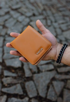 Brauner Leder Geldbeutel mit glatter Textur, abgerundeten Kanten und dem geprägten Markennamen "VUCH" auf der Vorderseite.