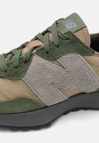 Baskets vertes et beiges avec une texture douce en daim, logo bien visible et semelle robuste. Lacets verts, col matelassé pour un meilleur maintien.