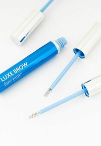 Blå sylinderformet tube for øyebryngel med sølvfarget kork, har hvit tekst "LUXE BROW." To blå applikatorer med spiralformede ender er inkludert.