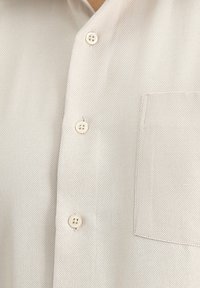 Camicia button-up beige chiaro con tessuto testurizzato, caratterizzata da quattro bottoni, una tasca a toppa e un design colletto classico.