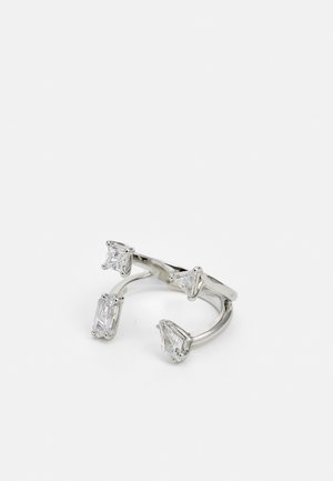 Otwarty srebrny pierścień z czterema dużymi przejrzystymi kamieniami szlachetnymi o trójkątnym, kwadratowym i prostokątnym szlifie na białym tle.