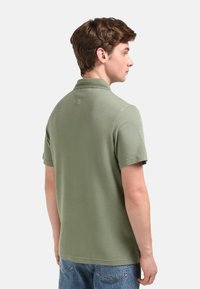 Polo de manga corta en algodón verde oliva claro, con un collar, detalle en la parte posterior y un dobladillo recto, combinado con jeans de mezclilla azul.