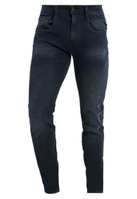 Miestne tmavomodré slim-fit džínsy s prednými vreckami, pútkami na opasok a zapínaním na gombík, vystavené na bielom pozadí.