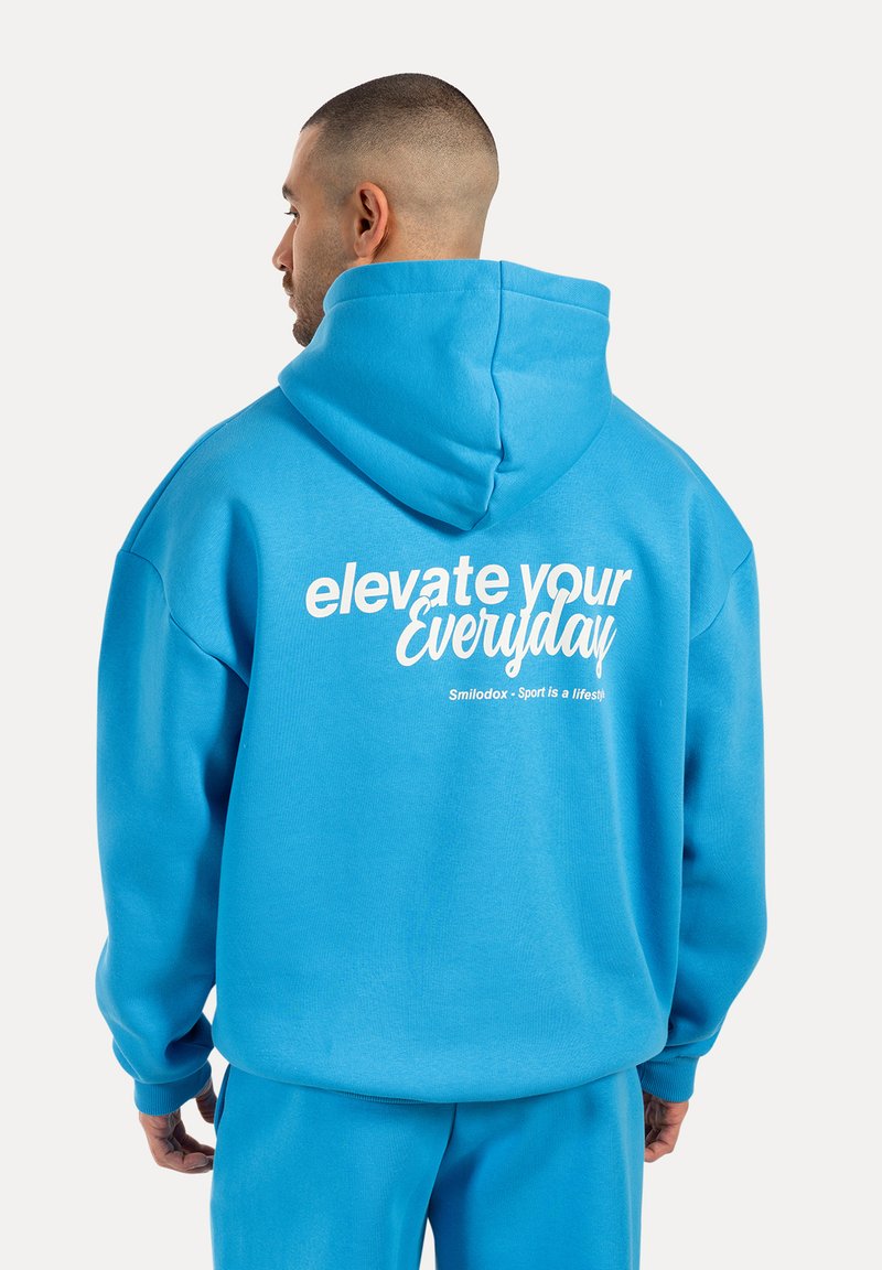 Hoodie en coton bleu avec une capuche à cordon de serrage, comportant un texte blanc au dos qui dit "élever votre quotidien" et des détails de logo.