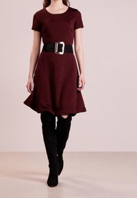 Vestido burdeos de manga corta con tela texturizada y un cinturón ancho negro con una gran hebilla plateada, combinado con botas negras hasta la rodilla.
