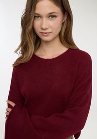 Maglione bordeaux con scollo ampio e rotondo e maniche lunghe. Realizzato in materiale morbido e strutturato, presenta una vestibilità comoda.