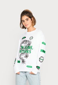 T-shirt de manga longa branca com um gráfico de dragão verde e vários detalhes de logotipo preto e verde nas mangas e na parte frontal. Corte desgastado.