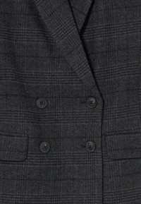 Blazer de doble botonadura en gris oscuro, hecho de lana texturizada con un patrón de cuadros, que presenta cuatro botones negros y dos bolsillos frontales.
