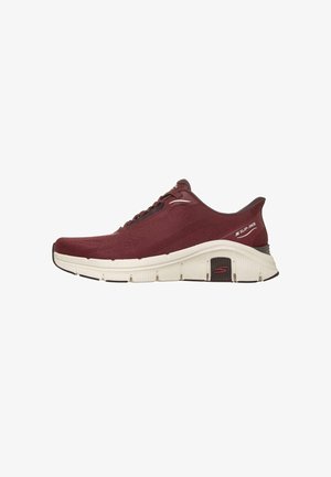 Zapatilla deportiva sin cordones color granate con suela blanca y detalles negros antideslizantes, parte superior de tejido ligero y etiqueta con la marca "SLIP-INS" en el talón.
