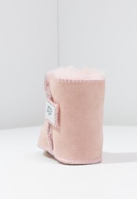 Rosa Wildleder-Ankle-Boot mit weichem Echtfellfutter, sichtbaren Nähten und einem gewebten Logolabel an der Seite. Gerundete Form und plüschige Textur.