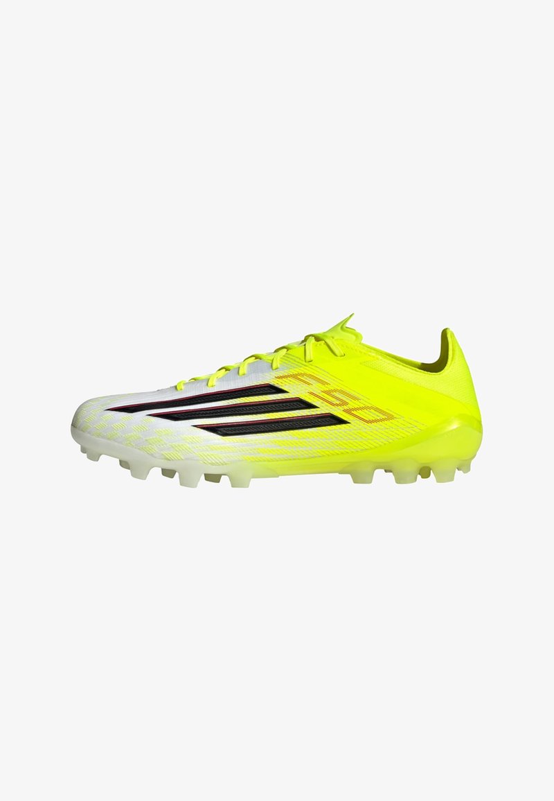 Φωτεινό κίτρινο ποδοσφαιρικό παπούτσι με συνθετικό επάνω μέρος, διακοσμημένο με μαύρες ρίγες και υφή σχεδίου. Περιλαμβάνει λευκές διαμορφωμένες τάπες για πρόσφυση.