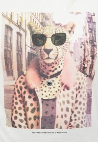 T-shirt blanc présentant un léopard portant des lunettes de soleil, une veste rose à pois et un collier, sur un fond urbain.