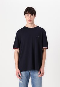 Marineblå kortærmet t-shirt med rund halsudskæring, der har røde og hvide stribede detaljer på ærmerne og et lille logo på brystet.