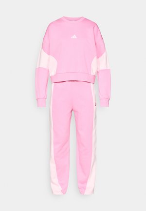 Conjunto de treino rosa composto por um sweatshirt cropped com detalhes em branco e calças combinando, ambos feitos de um tecido suave com um ajuste descontraído.