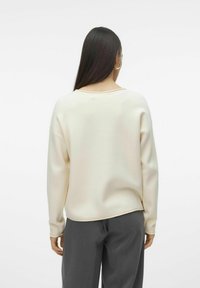 Sweatshirt crème clair avec une coupe décontractée, un col rond, des poignets côtelés et une texture douce. Associé à un pantalon gris ample.