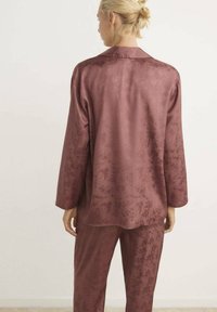 Bordeaux satin pyjamasæt med et blomstermønster, der inkluderer en langærmet top og løst siddende bukser, som fremhæver en glat tekstur og et elegant design.