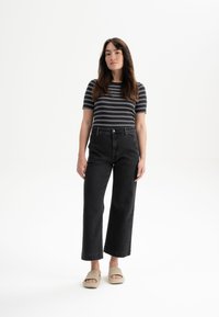 Zwarte wijde spijkerbroek, aansluitend gestreept shirt en beige slippers. De spijkerbroek heeft een hoge taille en een klassiek vijf-pocket ontwerp.