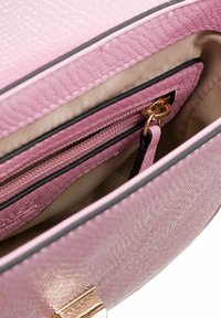 Roze getextureerde handtas met een ritscompartiment en een crèmekleurige voering. Bevat een gouden sluiting en zwarte randen rondom de bovenkant.