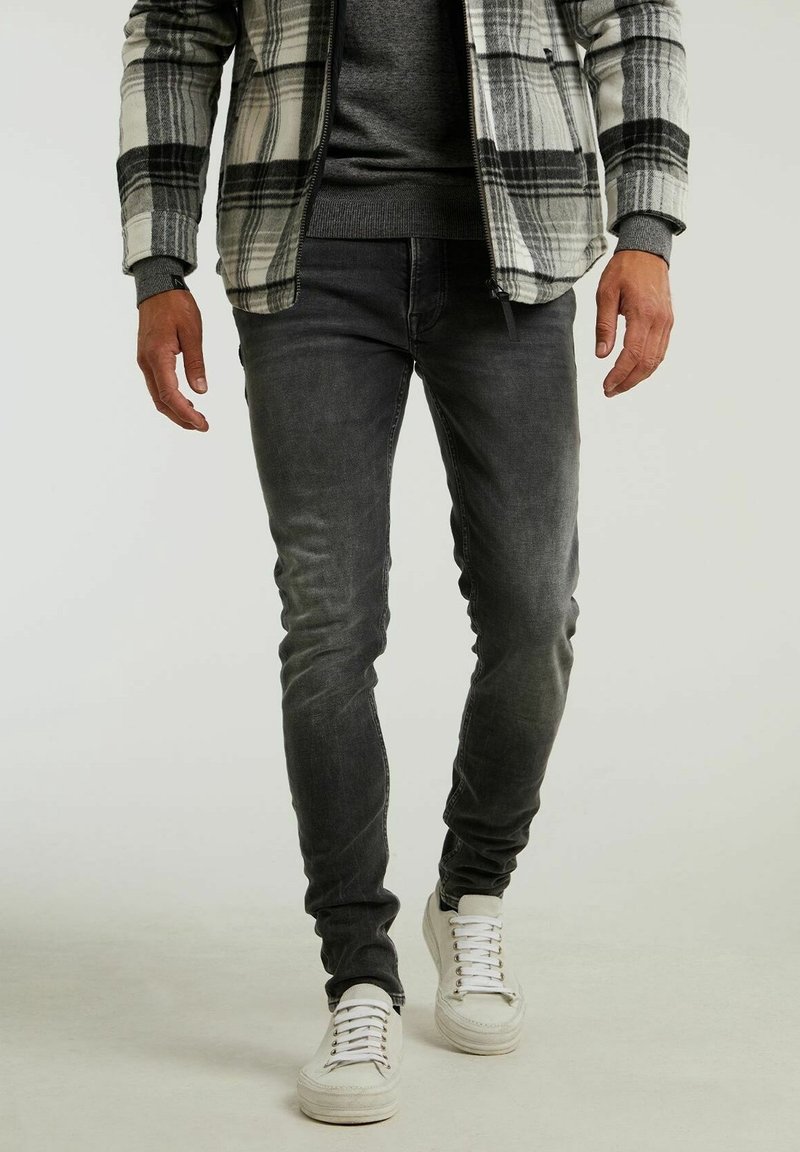Jeans ajustados grises de mezclilla, con un leve desgaste, combinados con zapatillas blancas. El conjunto incluye una chaqueta a cuadros en blanco y negro.